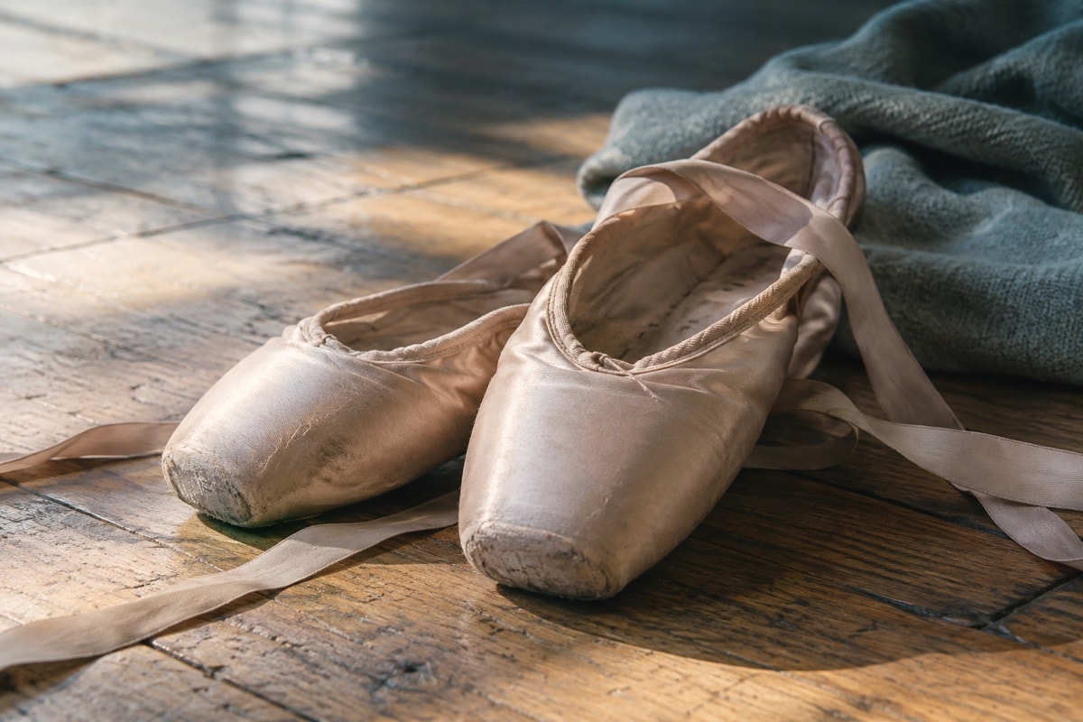 A pair of worn ballet pointe shoes on a wooden floor
